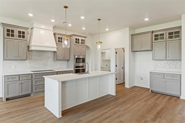 29744 Jade St, Cashion, OK 73016 - kitchen with gray cabinets, premium range hood, black electric cooktop, backsplash, and a center island with sink