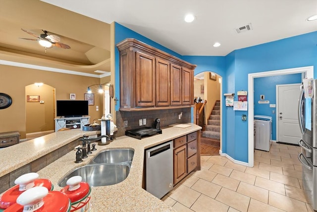 13117 SW 2nd Ter, Yukon, OK 73099 - kitchen with stainless steel appliances, arched walkways, washer / clothes dryer, brown cabinets, and backsplash
