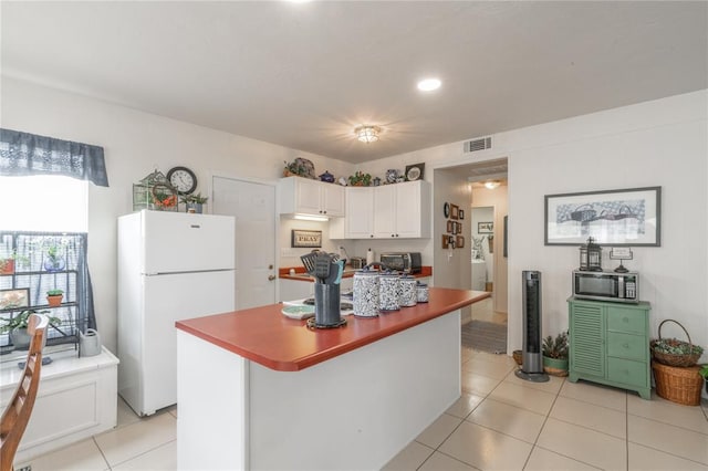 1300 Hutton Rd, Marlow, OK 73055 - kitchen featuring freestanding refrigerator, white cabinetry, stainless steel microwave, light tile patterned floors, and a center island