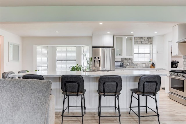 2401 Big Cedar Ave, Edmond, OK 73012 - kitchen featuring appliances with stainless steel finishes, a breakfast bar area, decorative backsplash, glass insert cabinets, and white cabinetry