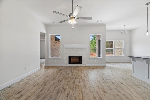 1244 Layla Ln, Blanchard, OK 73010 - unfurnished living room featuring light wood-style flooring, a stone fireplace, ceiling fan, and a chandelier