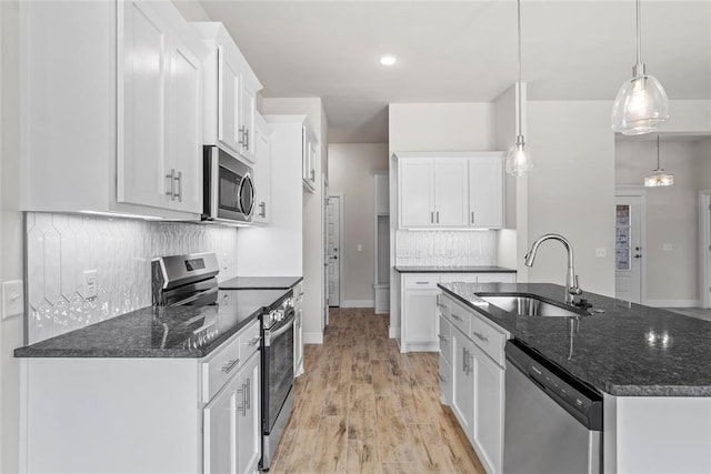 1244 Layla Ln, Blanchard, OK 73010 - kitchen with stainless steel appliances, a kitchen island with sink, backsplash, white cabinetry, and light wood-style flooring