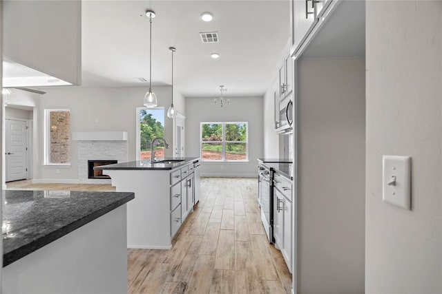 1244 Layla Ln, Blanchard, OK 73010 - kitchen with stainless steel appliances, light wood-style flooring, a center island with sink, a fireplace, and hanging light fixtures