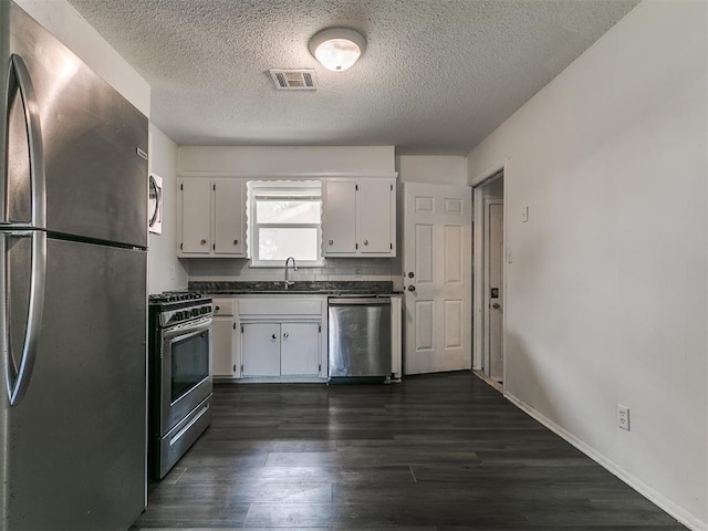 650 NW 5th St, Moore, OK 73160 - kitchen featuring appliances with stainless steel finishes, dark countertops, white cabinetry, a textured ceiling, and dark wood-style flooring