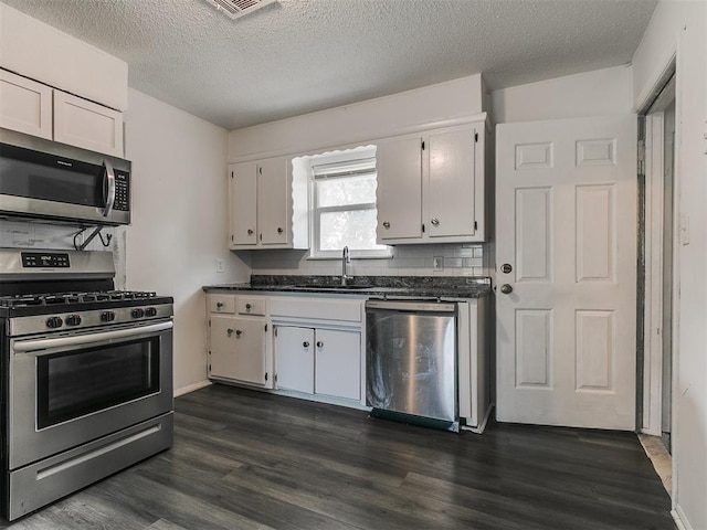 650 NW 5th St, Moore, OK 73160 - kitchen with appliances with stainless steel finishes, dark countertops, dark wood-style flooring, and a textured ceiling