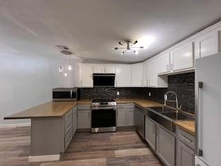 1727 NW 31st St, Oklahoma City, OK 73118 - kitchen featuring stainless steel appliances, a peninsula, decorative backsplash, light wood-style floors, and white cabinetry