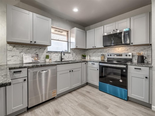 313 Ember Glow Dr, Moore, OK 73160 - kitchen with stainless steel appliances, decorative backsplash, light wood finished floors, dark stone counters, and recessed lighting