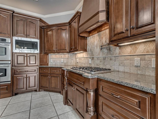 1233 Autumn Creek Dr, Edmond, OK 73003 - kitchen with stainless steel appliances, premium range hood, light stone counters, backsplash, and light tile patterned floors