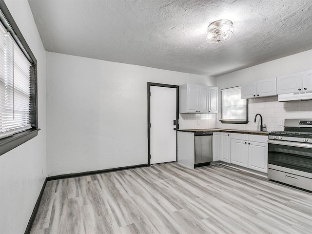 3225 SE 20th St, Oklahoma City, OK 73115 - kitchen with appliances with stainless steel finishes, under cabinet range hood, backsplash, dark countertops, and light wood-type flooring
