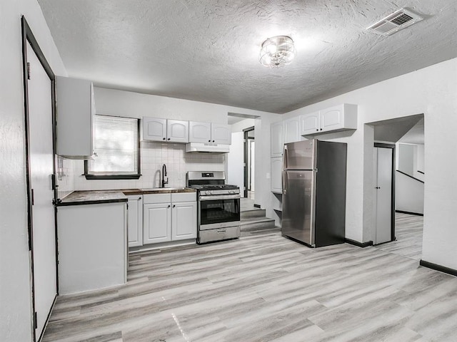 3225 SE 20th St, Oklahoma City, OK 73115 - kitchen featuring stainless steel appliances, under cabinet range hood, light wood-style flooring, a textured ceiling, and white cabinetry