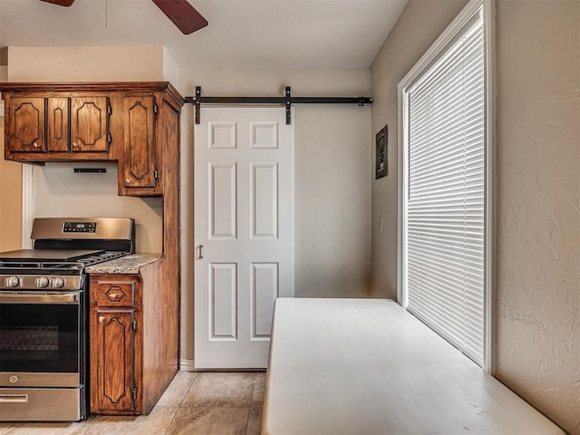 201 N Base Ave, Norman, OK 73069 - kitchen with stainless steel gas range oven, brown cabinets, ceiling fan, a barn door, and light countertops