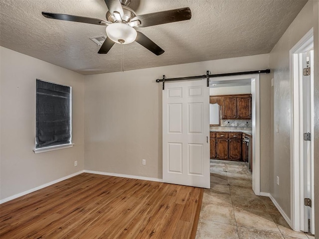 201 N Base Ave, Norman, OK 73069 - spare room featuring a textured ceiling, a ceiling fan, a barn door, and light wood-style floors