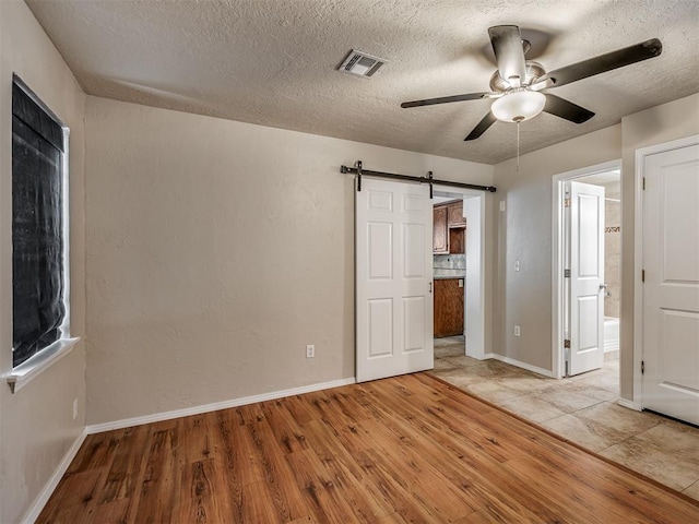 201 N Base Ave, Norman, OK 73069 - unfurnished bedroom featuring light wood-style flooring, ensuite bath, a barn door, a textured ceiling, and a ceiling fan