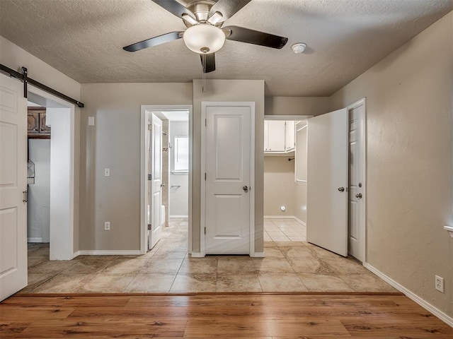 201 N Base Ave, Norman, OK 73069 - unfurnished bedroom with a textured ceiling, light wood-style floors, a barn door, connected bathroom, and ceiling fan
