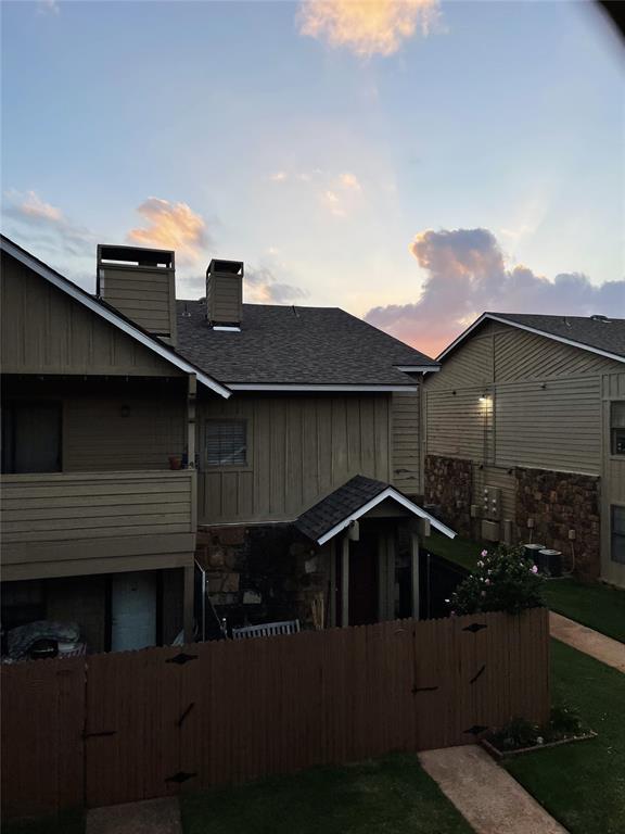 14313 N Pennsylvania Ave Unit 7E, Oklahoma City, OK 73134 - back of house at dusk with stone siding, a chimney, roof with shingles, and a gate