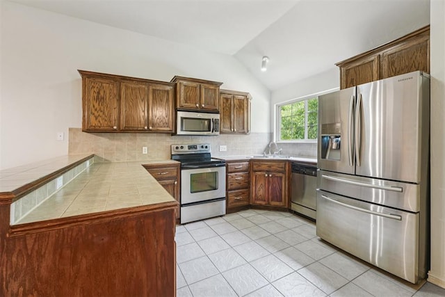 9716 SW 21st Ter, Oklahoma City, OK 73128 - kitchen featuring appliances with stainless steel finishes, a peninsula, vaulted ceiling, decorative backsplash, and light tile patterned flooring