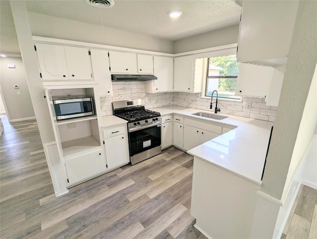 104 SW 10th St, Moore, OK 73160 - kitchen with stainless steel appliances, under cabinet range hood, a textured ceiling, decorative backsplash, and light wood-style flooring