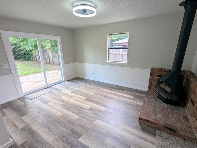 104 SW 10th St, Moore, OK 73160 - unfurnished living room featuring a wood stove, a textured ceiling, a wainscoted wall, wood finished floors, and a ceiling fan