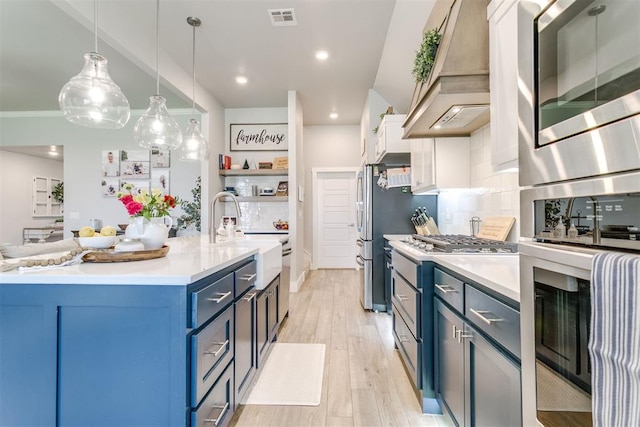 10125 NW 99th St, Yukon, OK 73099 - kitchen with custom range hood, blue cabinetry, appliances with stainless steel finishes, light countertops, and light wood-style flooring