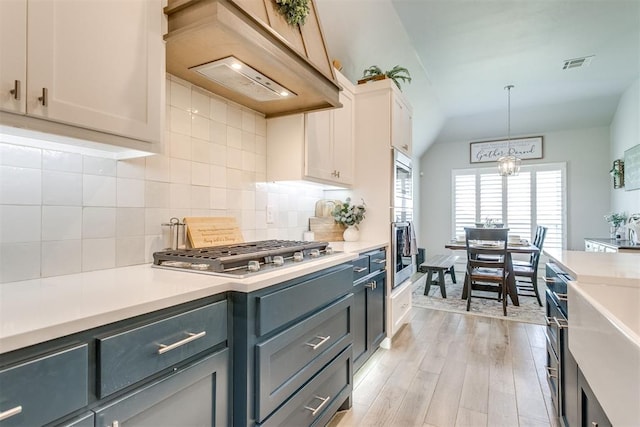 10125 NW 99th St, Yukon, OK 73099 - kitchen with appliances with stainless steel finishes, custom range hood, light countertops, backsplash, and light wood-type flooring