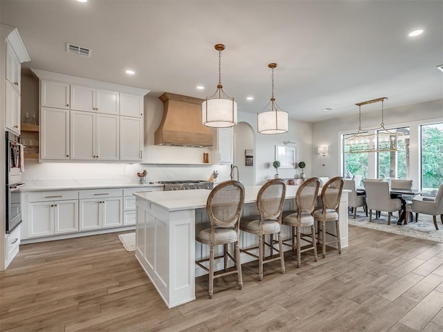 19890 Hickory Ridge Rd, Arcadia, OK 73007 - kitchen with custom exhaust hood, light countertops, light wood finished floors, an island with sink, and recessed lighting
