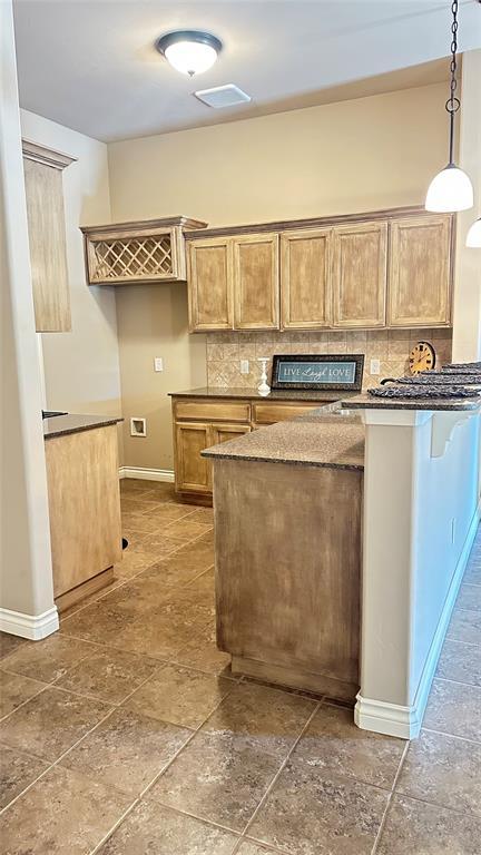 kitchen with backsplash, pendant lighting, a peninsula, and stone tile floors