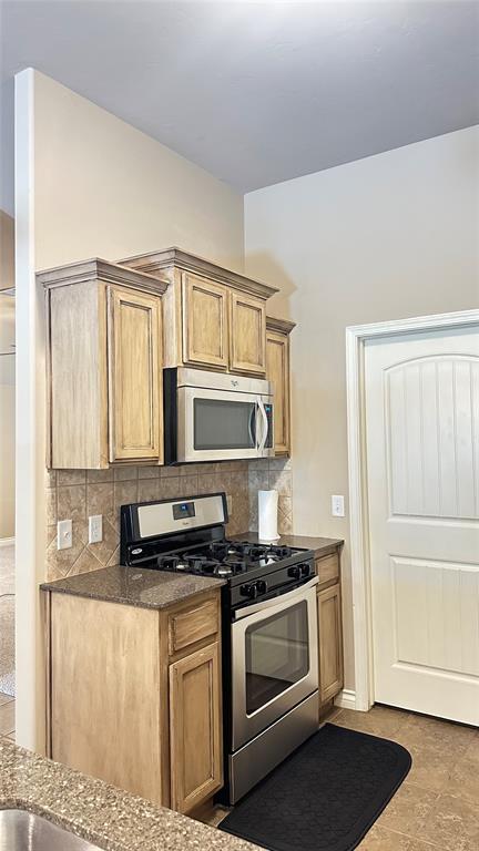 kitchen featuring appliances with stainless steel finishes, decorative backsplash, dark stone countertops, and brown cabinets