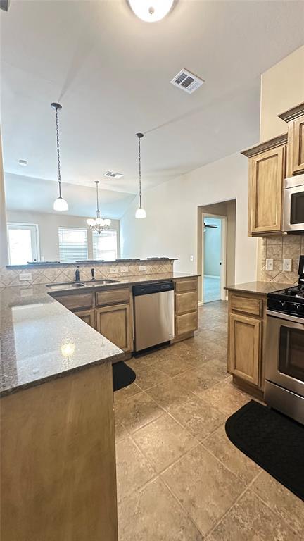 kitchen featuring appliances with stainless steel finishes, backsplash, hanging light fixtures, brown cabinetry, and dark stone countertops