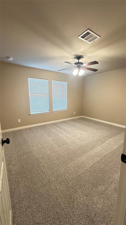 carpeted spare room with a ceiling fan and baseboards