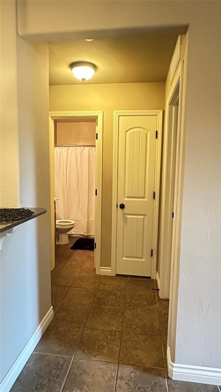 hallway featuring baseboards and dark tile patterned flooring