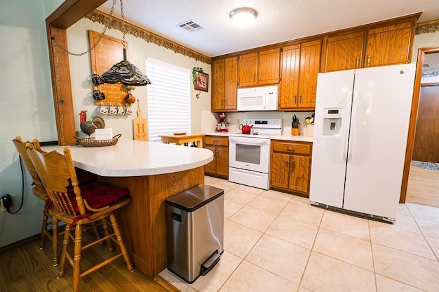 207 S Mcclure Ave, Pauls Valley, OK 73075 - kitchen featuring white appliances, brown cabinetry, light countertops, a peninsula, and a kitchen bar