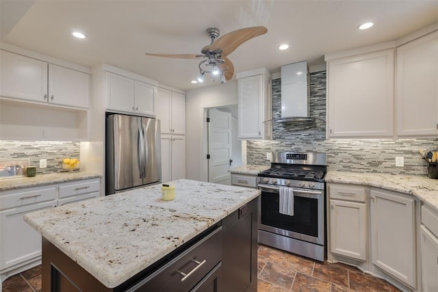 615 NW 26th St, Oklahoma City, OK 73103 - kitchen featuring stainless steel appliances, wall chimney range hood, a ceiling fan, decorative backsplash, and white cabinets
