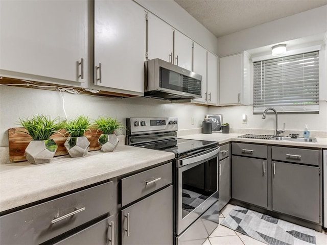 501 E Cardinal Pl, Midwest City, OK 73130 - kitchen with stainless steel appliances, gray cabinets, light countertops, light tile patterned flooring, and white cabinets