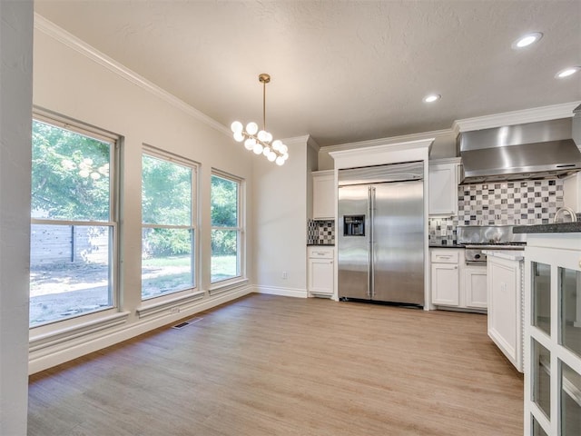 1008 Bentbrook Pl, Norman, OK 73072 - kitchen with stainless steel built in refrigerator, wall chimney exhaust hood, tasteful backsplash, crown molding, and healthy amount of natural light