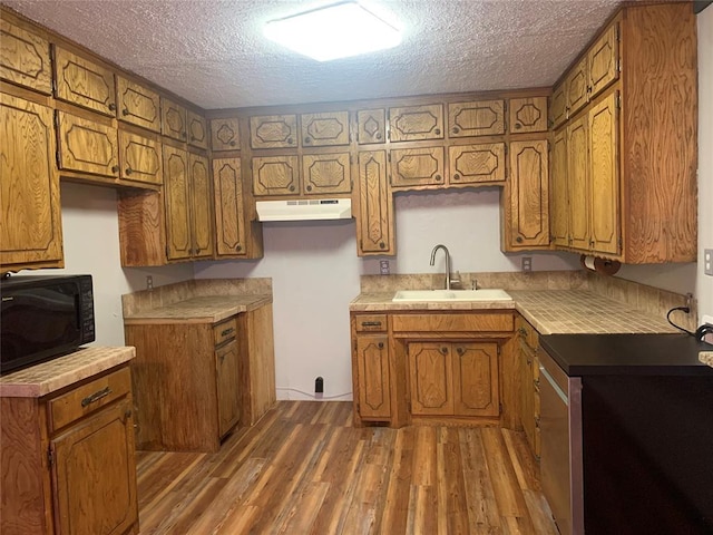 28153 County Street 2540Th, St, Fort Cobb, OK 73038 - kitchen featuring black microwave, under cabinet range hood, brown cabinetry, wood finished floors, and a textured ceiling