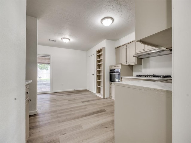 3044 S Madole Blvd, Oklahoma City, OK 73159 - kitchen featuring appliances with stainless steel finishes, a textured ceiling, light countertops, light wood-style flooring, and under cabinet range hood