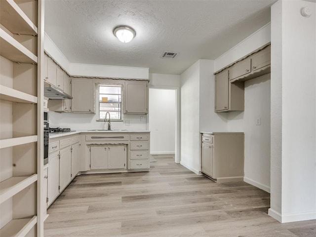 3044 S Madole Blvd, Oklahoma City, OK 73159 - kitchen with stainless steel gas stovetop, under cabinet range hood, a textured ceiling, light wood-type flooring, and light countertops
