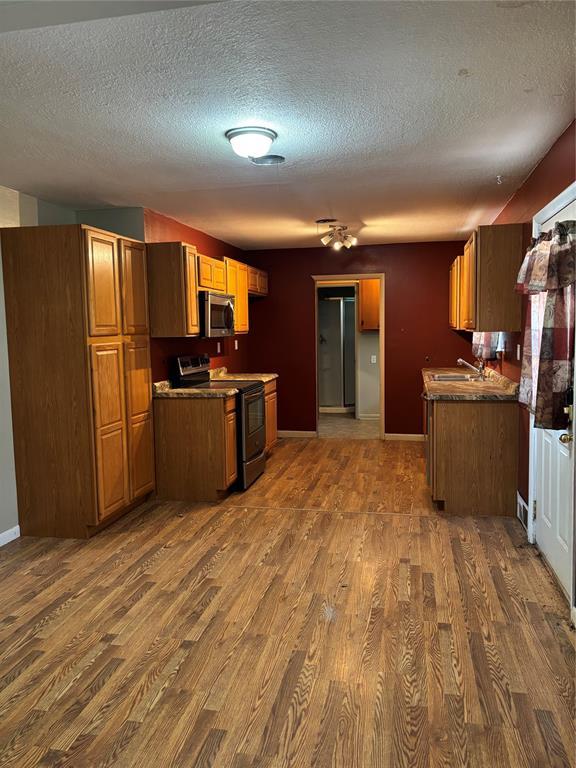 611 Garth Brooks Blvd, Yukon, OK 73099 - kitchen featuring appliances with stainless steel finishes, dark wood-type flooring, a textured ceiling, brown cabinetry, and dark countertops