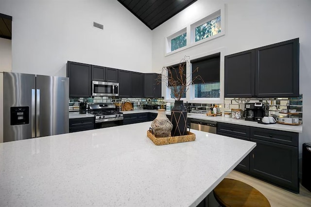 156 Butternut Trl, Broken Bow, OK 74728 - kitchen with appliances with stainless steel finishes, high vaulted ceiling, dark cabinetry, decorative backsplash, and light stone countertops