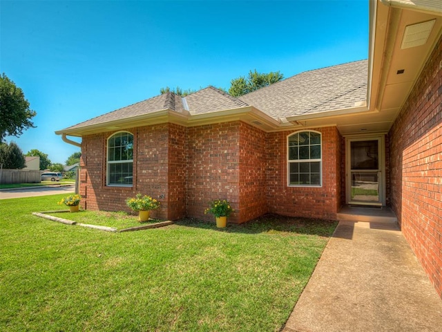 400 Ryan Way, Edmond, OK 73003 - view of exterior entry with roof with shingles, brick siding, and a lawn