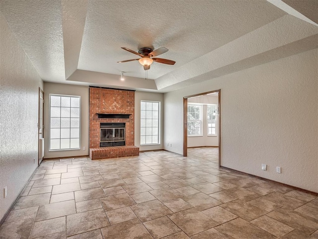 400 Ryan Way, Edmond, OK 73003 - unfurnished living room with a textured wall, a tray ceiling, a textured ceiling, ceiling fan, and a brick fireplace