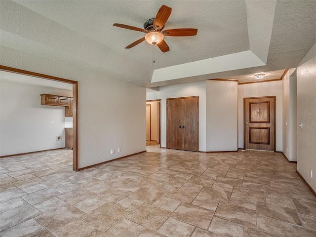 400 Ryan Way, Edmond, OK 73003 - empty room featuring light stone finish flooring, a ceiling fan, a raised ceiling, and a textured ceiling