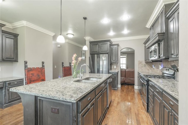 9409 NW 91st St, Yukon, OK 73099 - kitchen featuring appliances with stainless steel finishes, arched walkways, light wood-style floors, a kitchen island with sink, and light stone counters