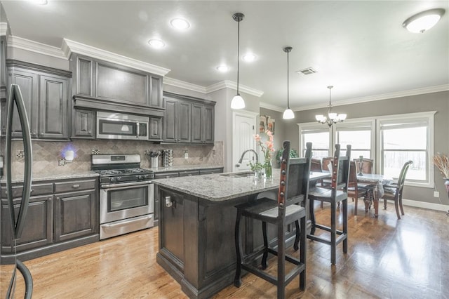 9409 NW 91st St, Yukon, OK 73099 - kitchen featuring appliances with stainless steel finishes, light stone counters, tasteful backsplash, a chandelier, and light wood finished floors