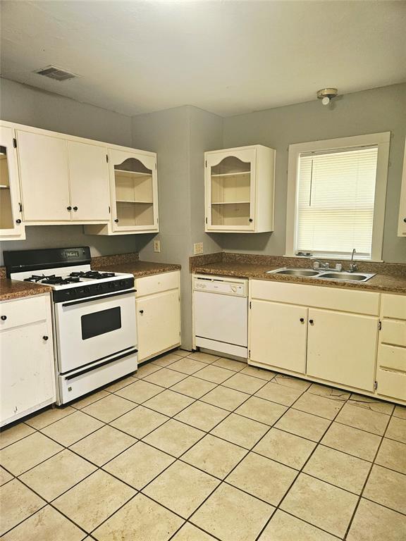 934 E Elm St, Altus, OK 73521 - kitchen featuring white appliances, dark countertops, light tile patterned floors, and white cabinetry