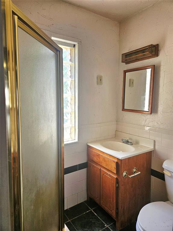 934 E Elm St, Altus, OK 73521 - bathroom with tile walls, vanity, a shower stall, tile patterned flooring, and a wainscoted wall