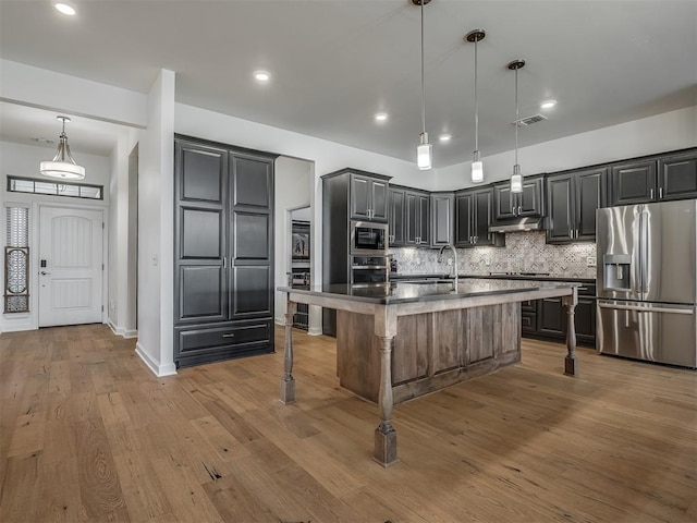 3760 Black Mesa Rd, Norman, OK 73071 - kitchen featuring appliances with stainless steel finishes, a breakfast bar, decorative backsplash, wood finished floors, and an island with sink