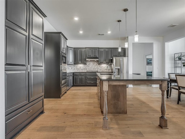 3760 Black Mesa Rd, Norman, OK 73071 - kitchen featuring stainless steel appliances, dark countertops, backsplash, light wood-style flooring, and pendant lighting