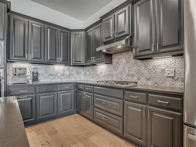 3760 Black Mesa Rd, Norman, OK 73071 - kitchen with appliances with stainless steel finishes, under cabinet range hood, light wood finished floors, dark countertops, and backsplash