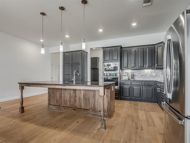 3760 Black Mesa Rd, Norman, OK 73071 - kitchen with appliances with stainless steel finishes, decorative backsplash, an island with sink, light wood-style floors, and recessed lighting